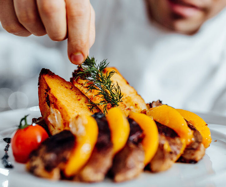 A chef places a garnish on a plate of food