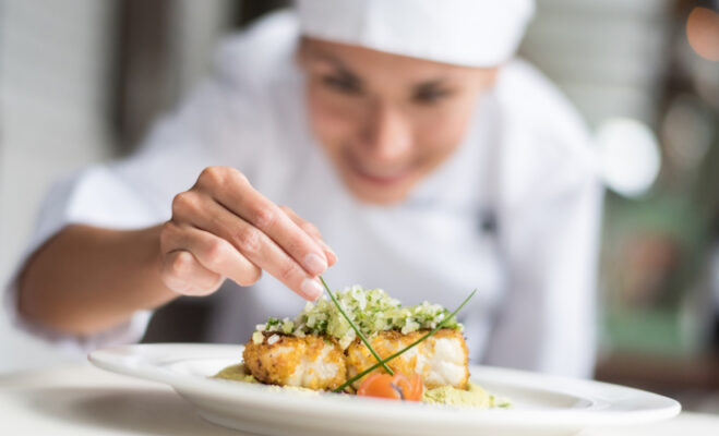 Cook decorating a plate and putting the finishing touches - focus on foreground