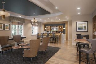 View of a library within a senior living community including chairs for conversation and a bar
