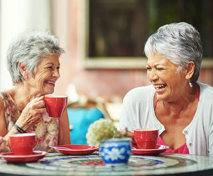 Two senior women laugh together while enjoying a cup of coffee