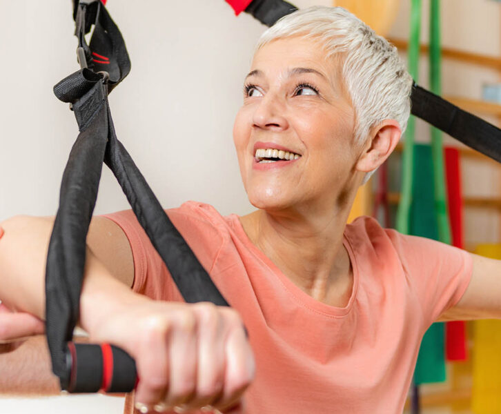 Senior woman training arms with trx fitness straps in the gym with coach’s help