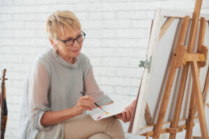 Senior woman painting at an easel. Art therapy offers significant benefits to both psychological and physical well-being.