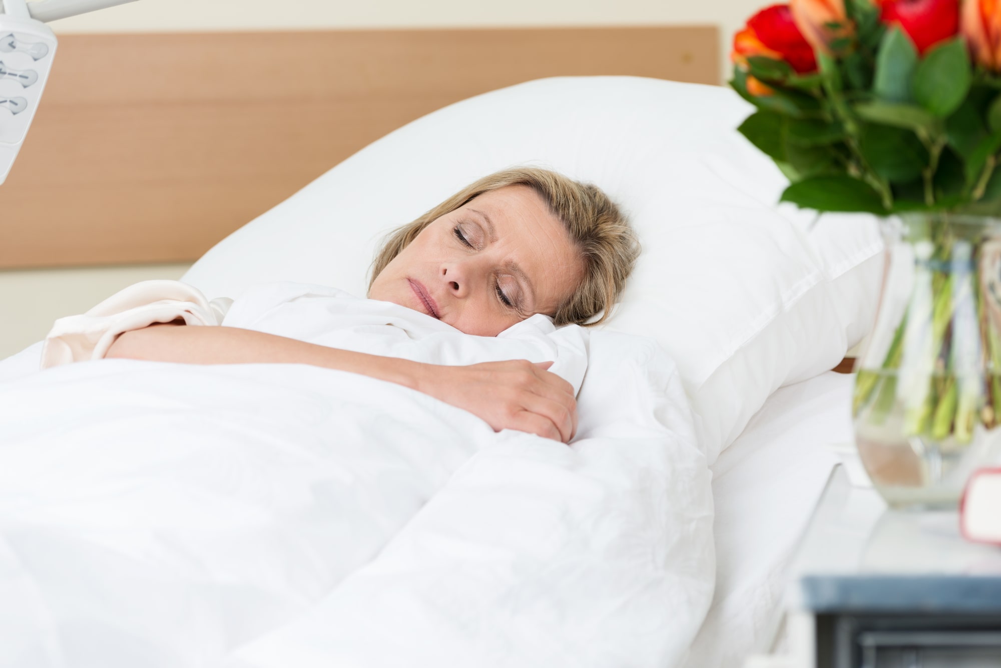 Woman sleeping peacefully in a hospital bed next to roses symbolizing recovery.