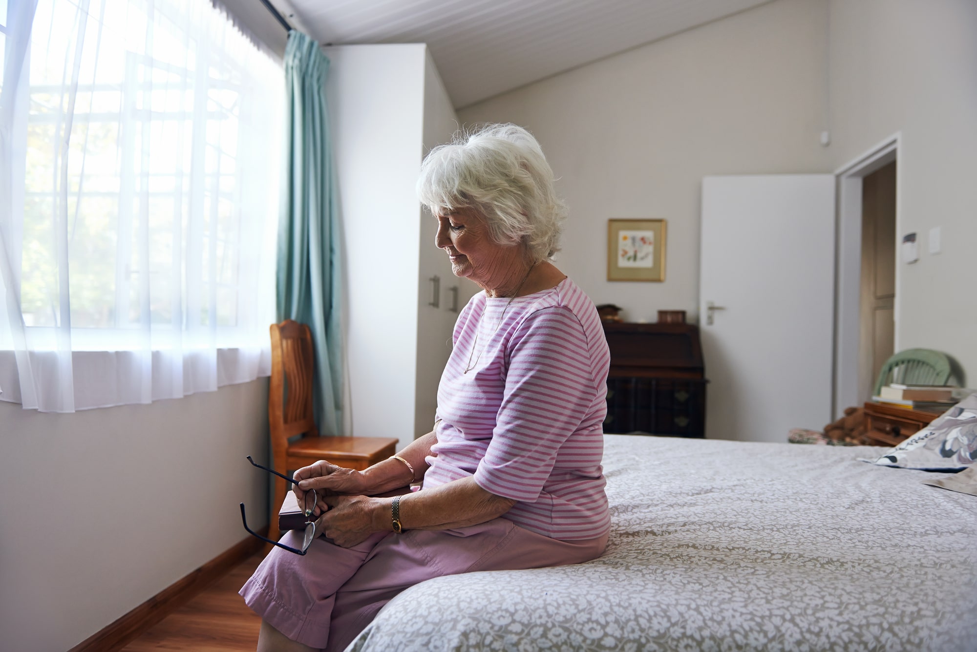 Lonely senior woman sitting in bedroom looking sad.