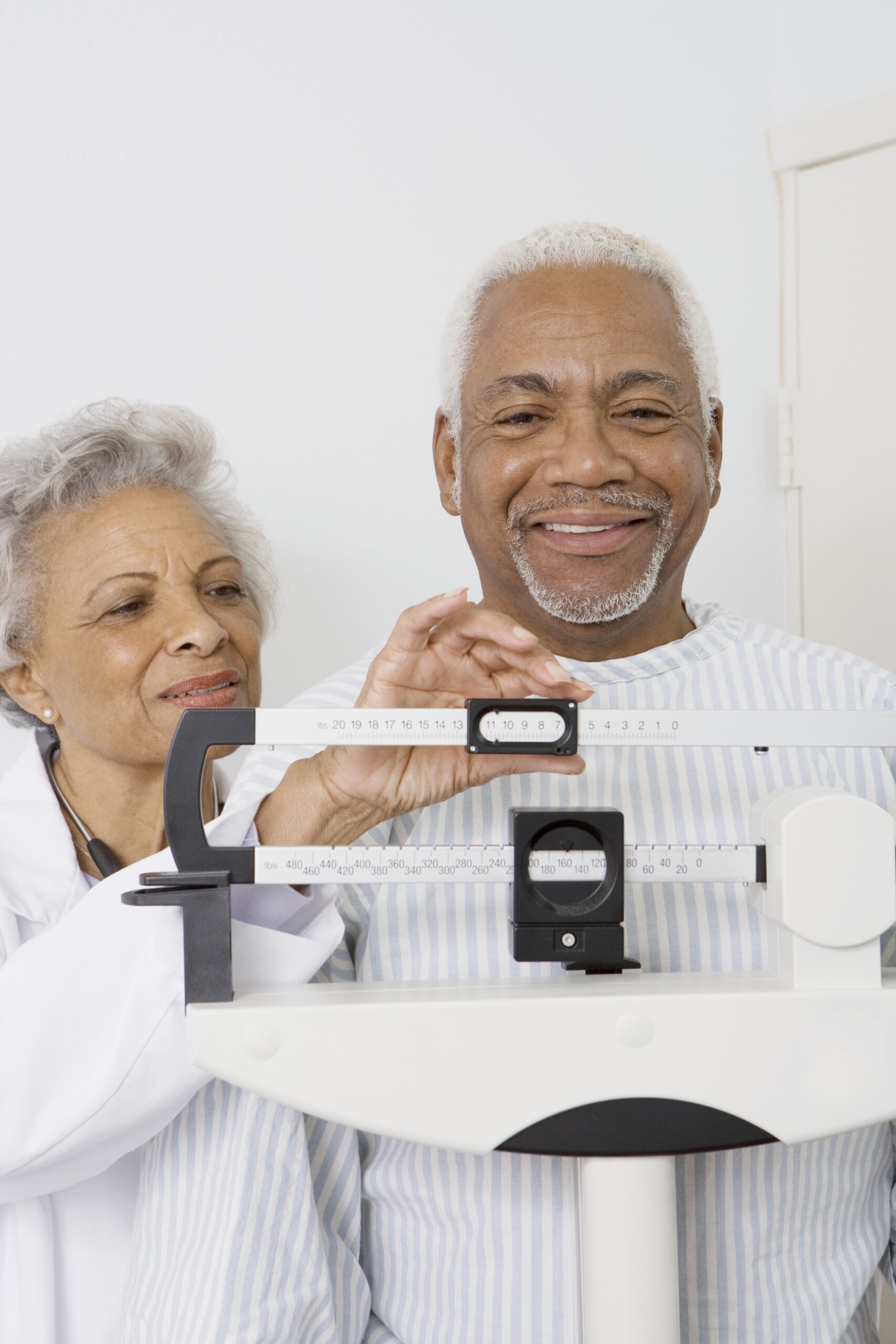 Smiling senior man stepping on a scale standing next to a doctor.
