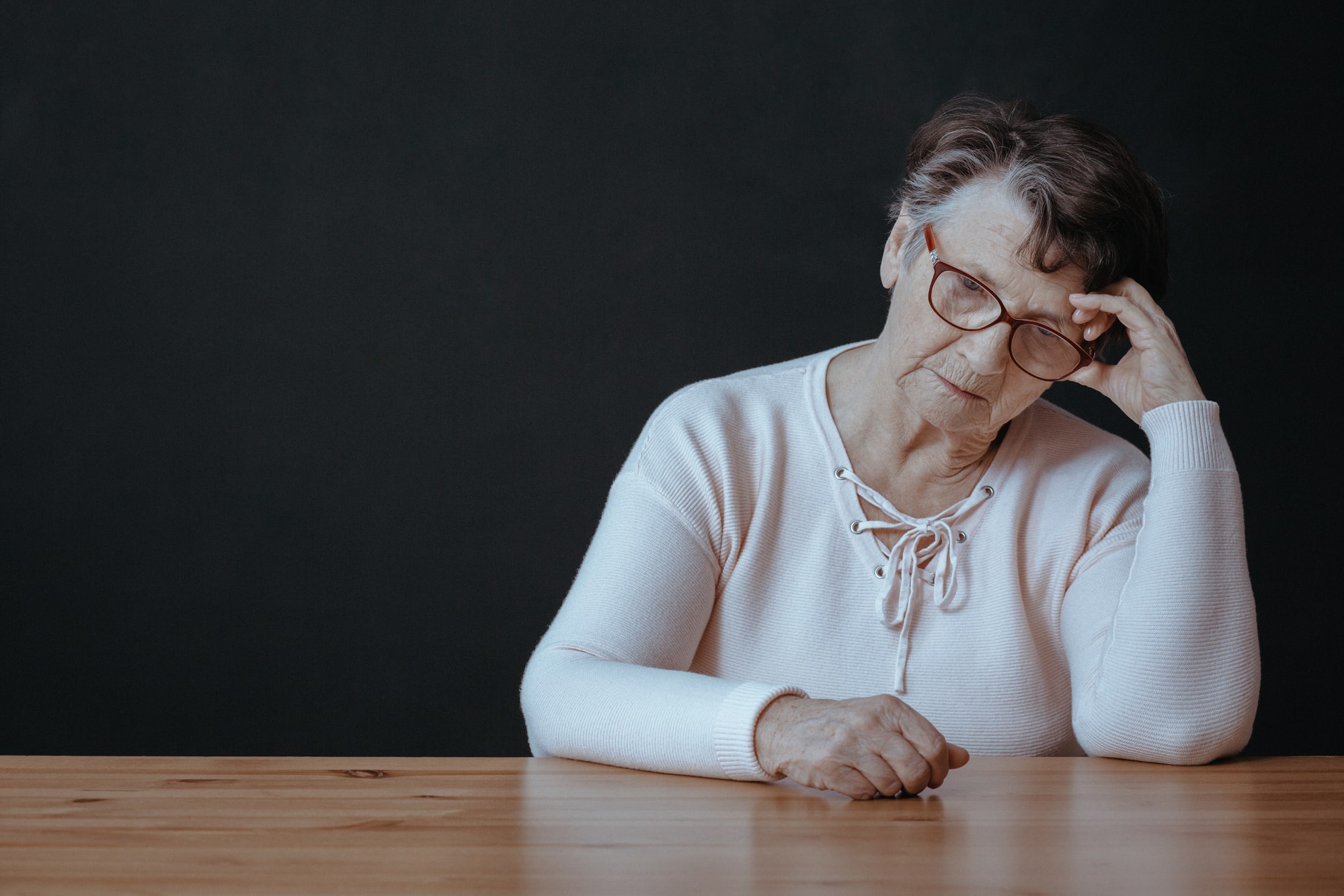 Image of a sad senior woman sitting at a table.