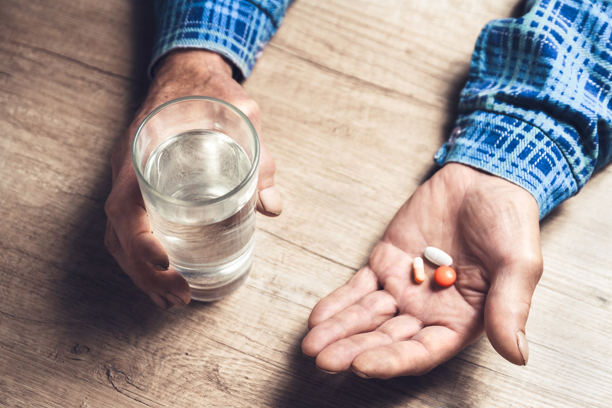 Senior male holding medications and a glass of water.